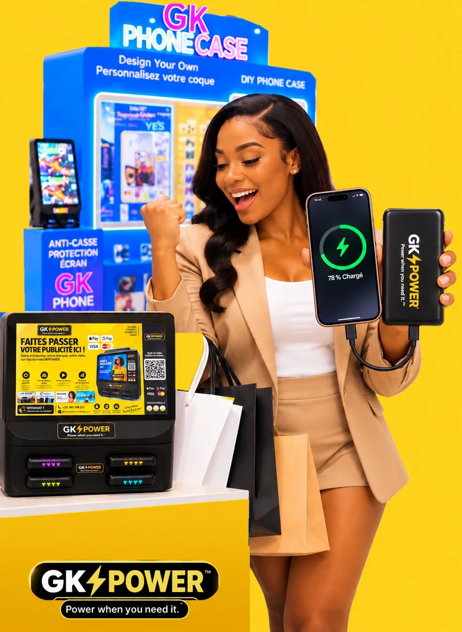 Une femme souriante montre son téléphone en charge, relié à une batterie GK POWER, devant les machines GK PHONECASE et GK POWER
